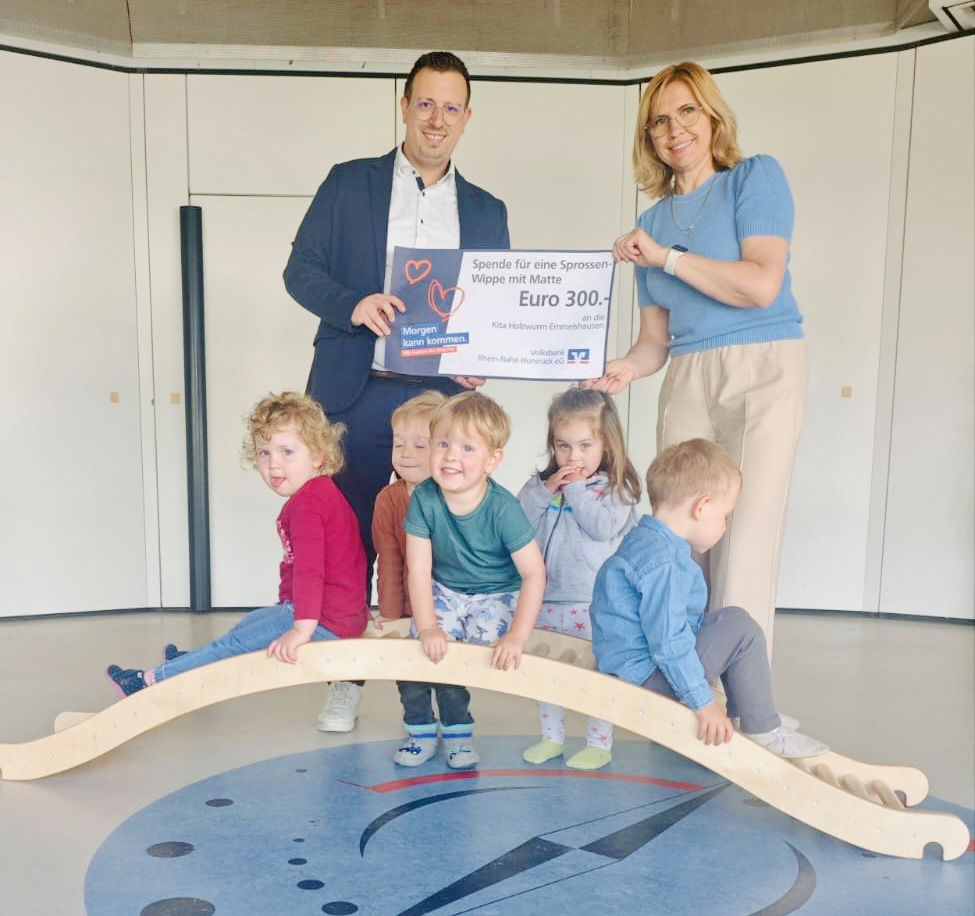 Erwachsene halten einen Spendenscheck in der Hand. Kinder spielen auf einer Holzbrücke.