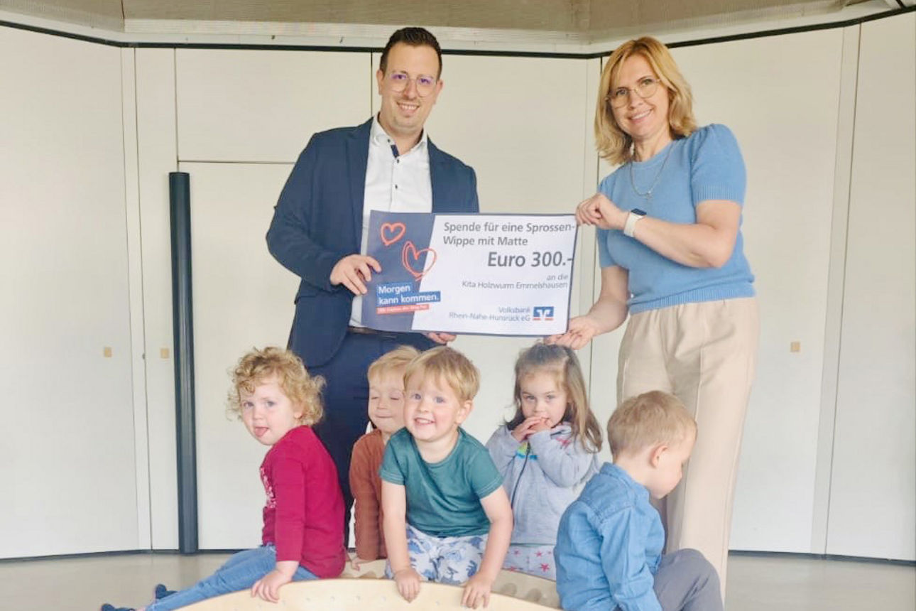 Erwachsene halten einen Spendenscheck in der Hand. Kinder spielen auf einer Holzbrücke.