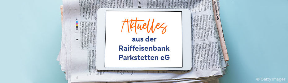 Eine Zeitung, auf der ein Tablet liegt. Das Tablet zeigt die Aufschrift "Aktuelles aus der Raiffeisenbank Parkstetten eG"