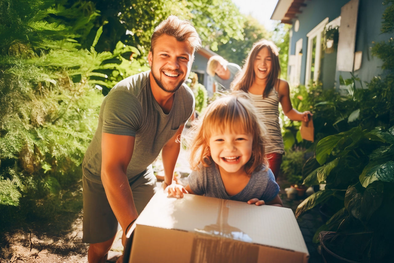 Auf dem Bild ist eine junge Familie mit einem Kind zu sehen, das vor einem Karton sitzt.