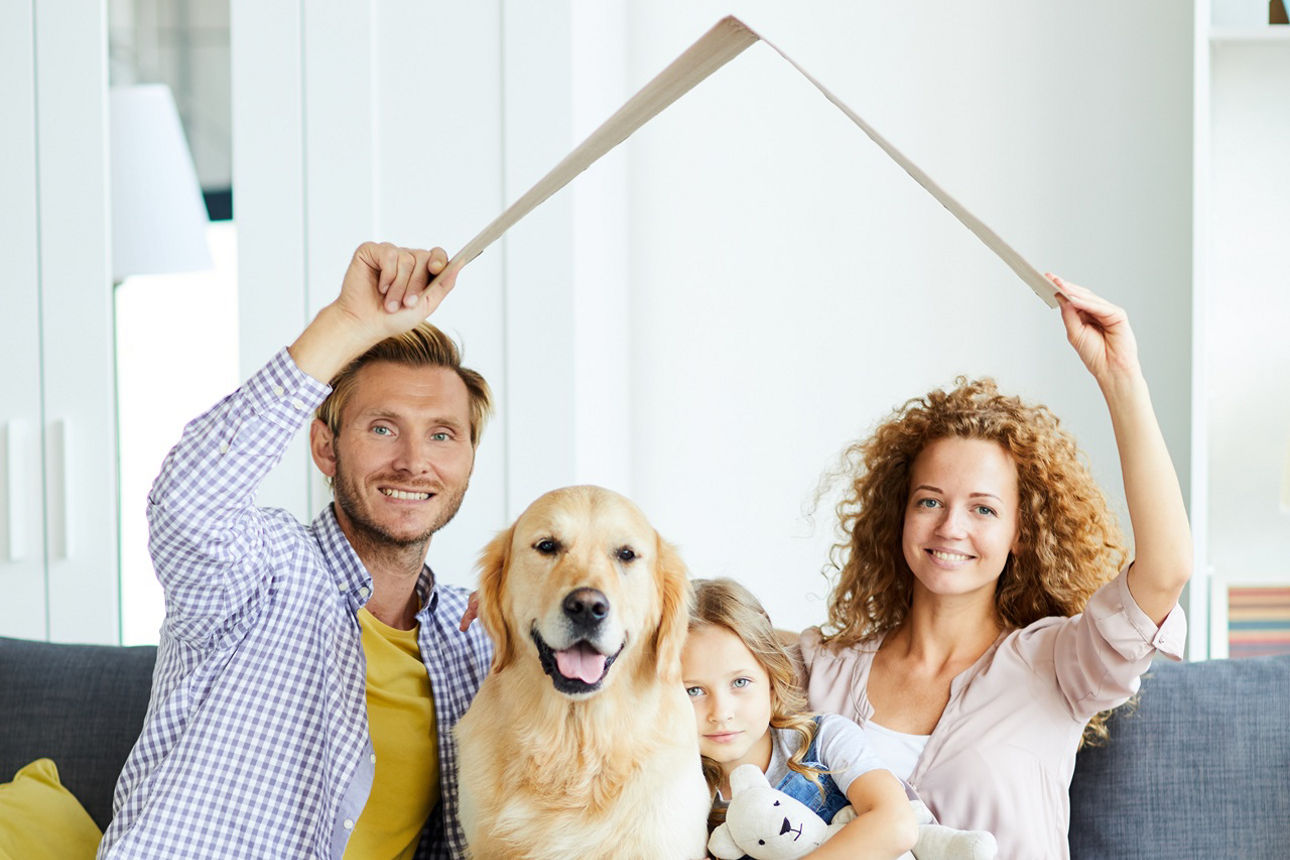 Dreiköpfige Familie mit Hund auf dem Sofa unter einem imaginären Pappdach.