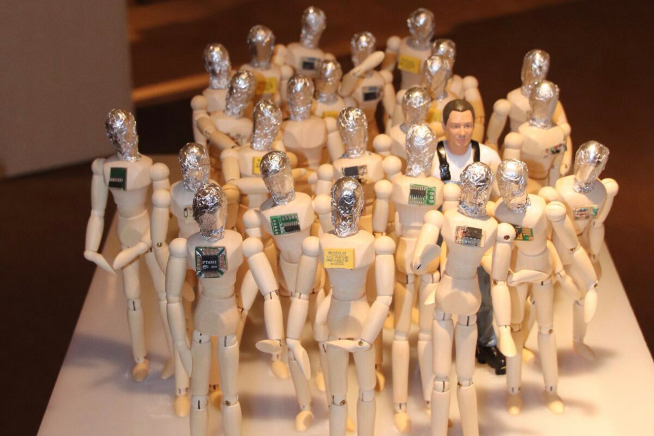 Holzfiguren, deren Köpfe mit Alufolie umwickelt sind, blicken frontal in die Kamera