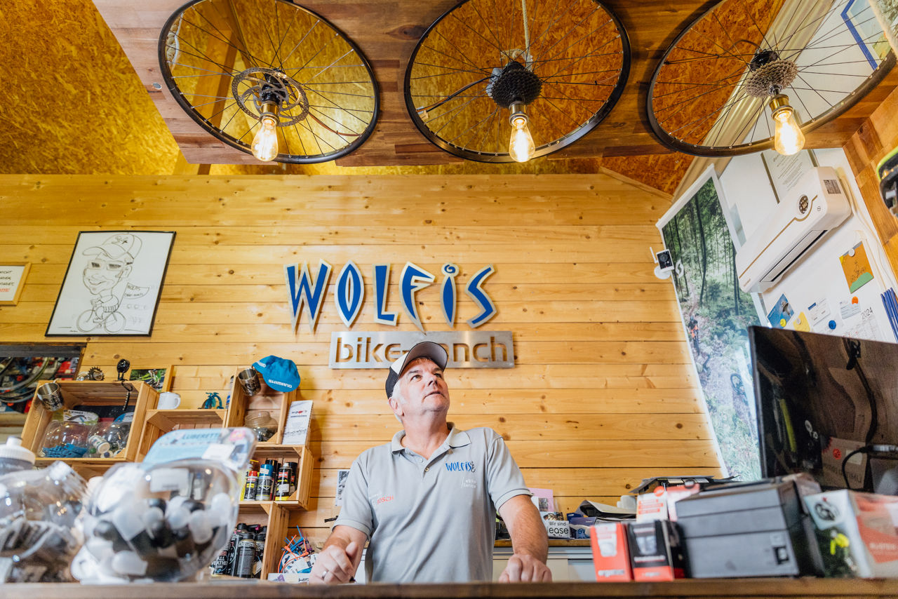 Innenaufnahme des Kassen‑ und Servicebereichs von Wolfis Bike Ranch mit Ladentheke, Fahrraddekoration und sichtbarem Markenlogo an der Wand. Die Aufnahme zeigt den zentralen Anlaufpunkt im Geschäft.