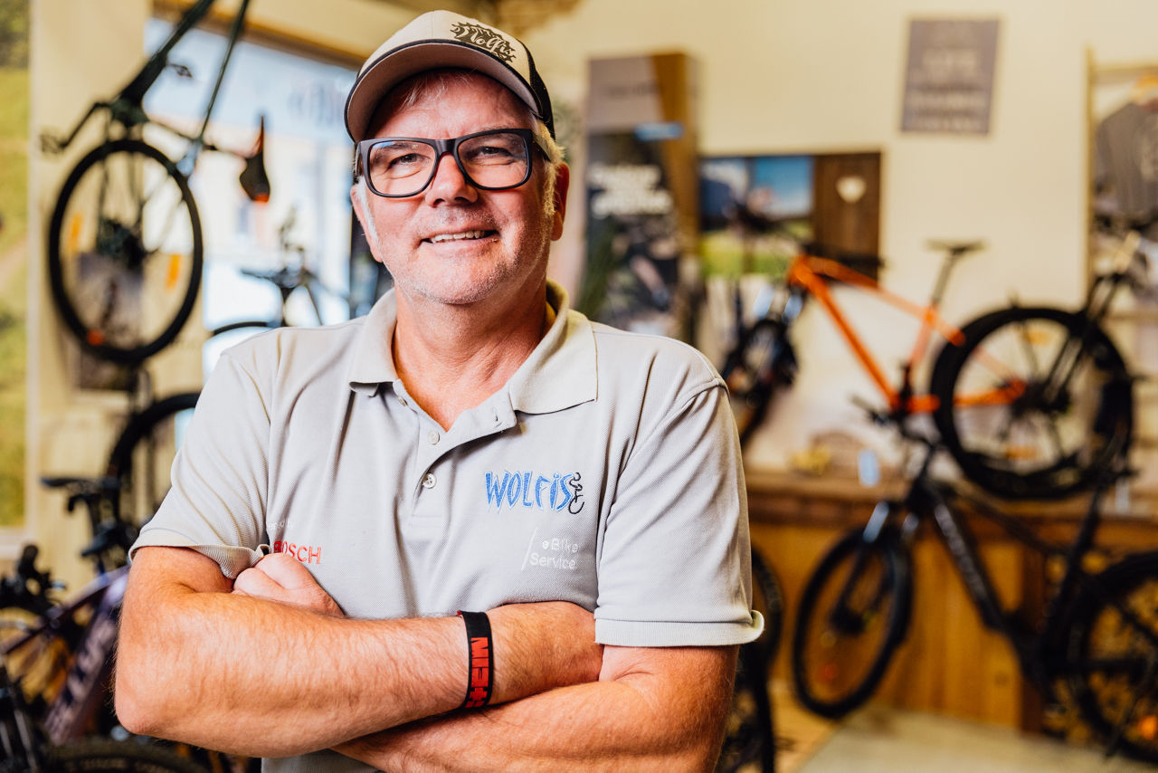 Wolfgang Brand im Innenbereich von Wolfis Bike Ranch, umgeben von ausgestellten Fahrrädern und Zubehör. Der Fokus liegt auf dem Verkaufsraum und der Sortimentsvielfalt.