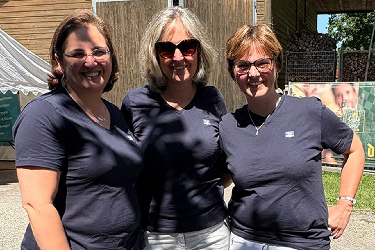 Drei Frauen stehen in der Sonne und lachen.