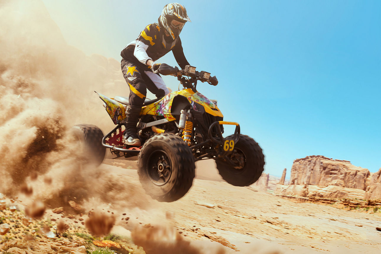 Mann sitzt auf dem Quad und fährt durch die Wüste, es staubt.