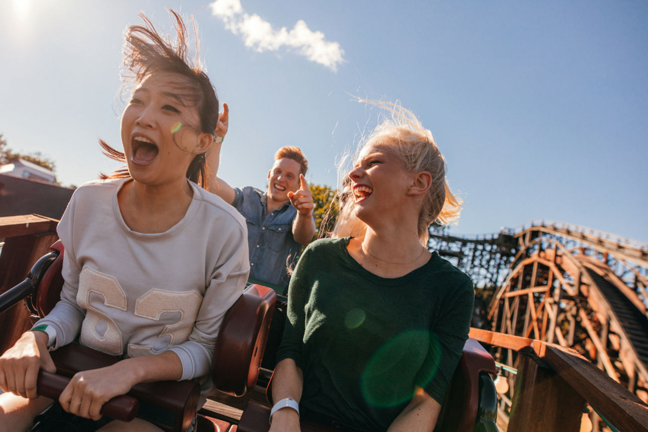 Zwei Mädchen und ein Junge fahren Achterbahn, lachen und haben Spaß