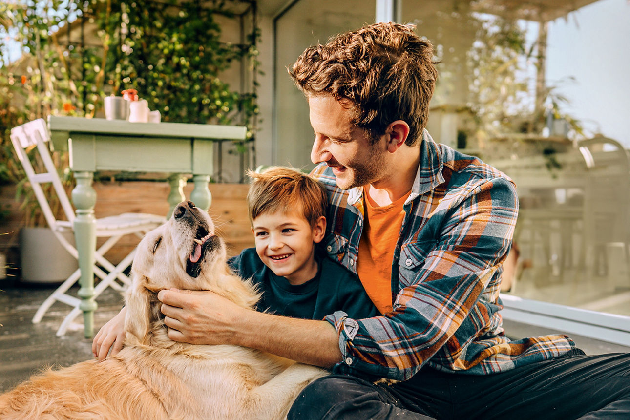 Ein Mann sitzt mit einem Kind aud dem Boden und beide steicheln dabei einen Hund.