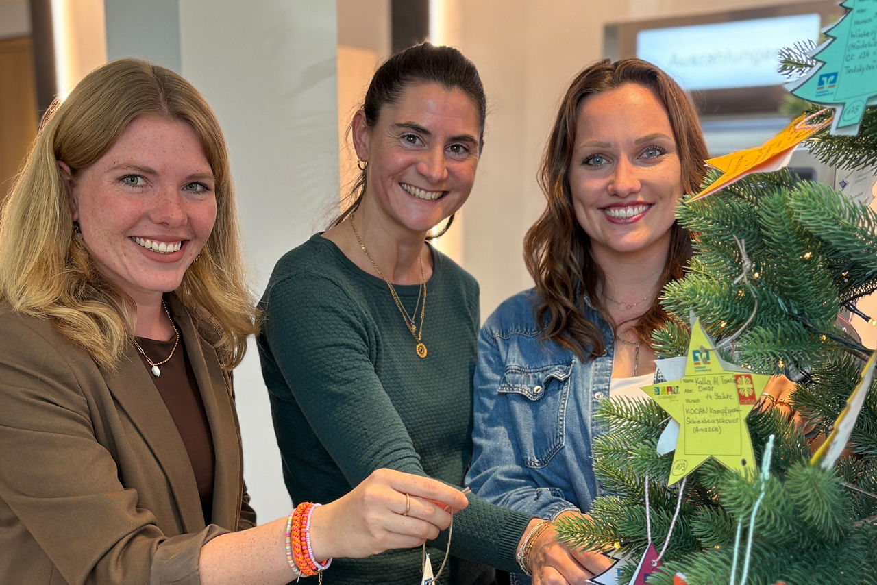 Drei Frauen stehen lächelnd neben einem Weihnachtsbaum