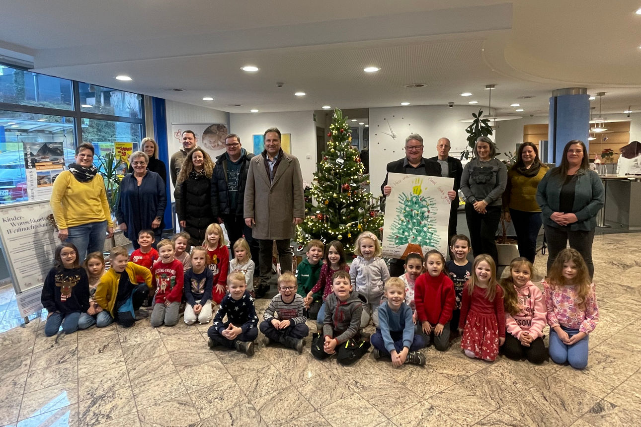 Gruppe aus Kindern und Erwachsenen steht um einen Weihnachtsbaum