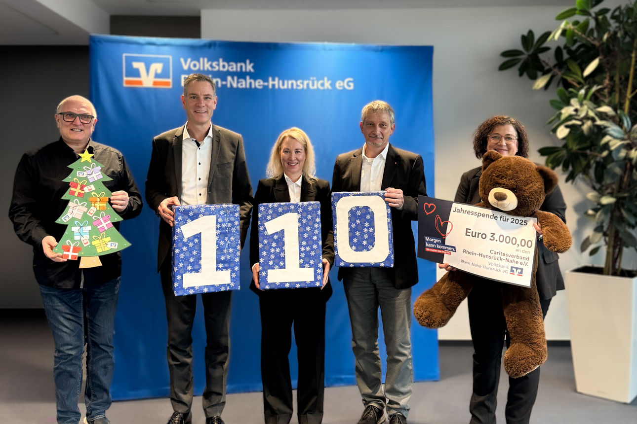 Eine Gruppe von Erwachsenen halten die Zahl 110 als Geschenk verpackt und stehen vor einer blauen Wand.