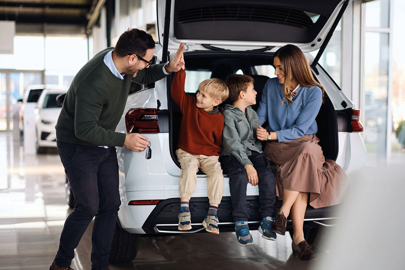 Im Auto hinten mit offener Kofferraumklappe sitzen zwei Kinder und zwei errwachsene Personen.