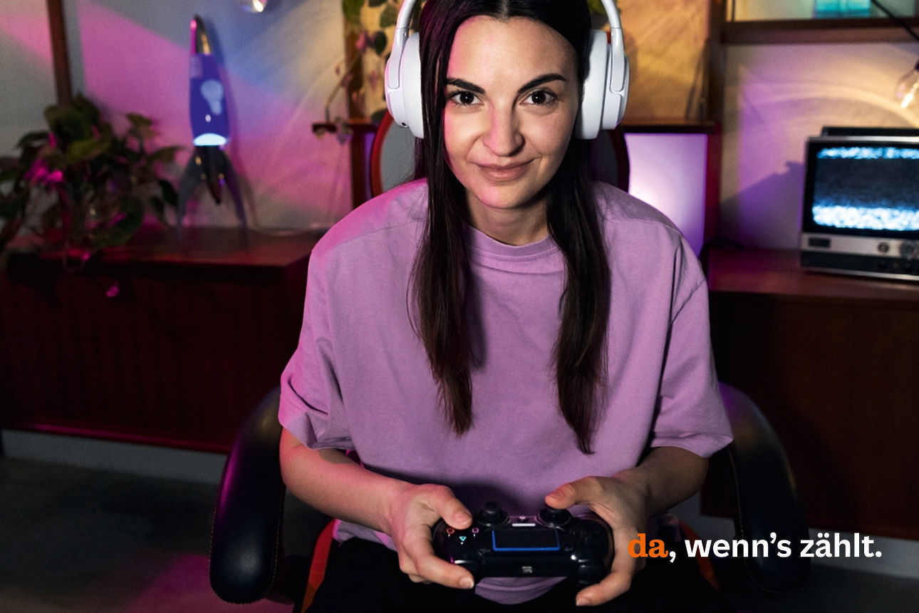 Eine Frau spielt eine Konsolenspiel und blickt dabei in die Kamera.
