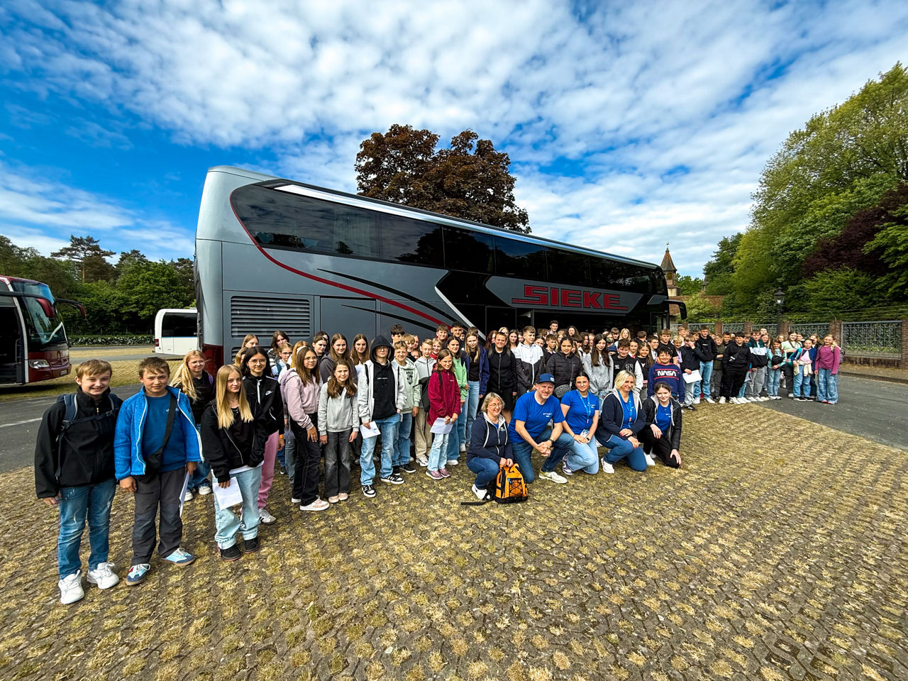 Eine große Kindergruppe steht auf einem Parkplatz vor einem Reisebus.