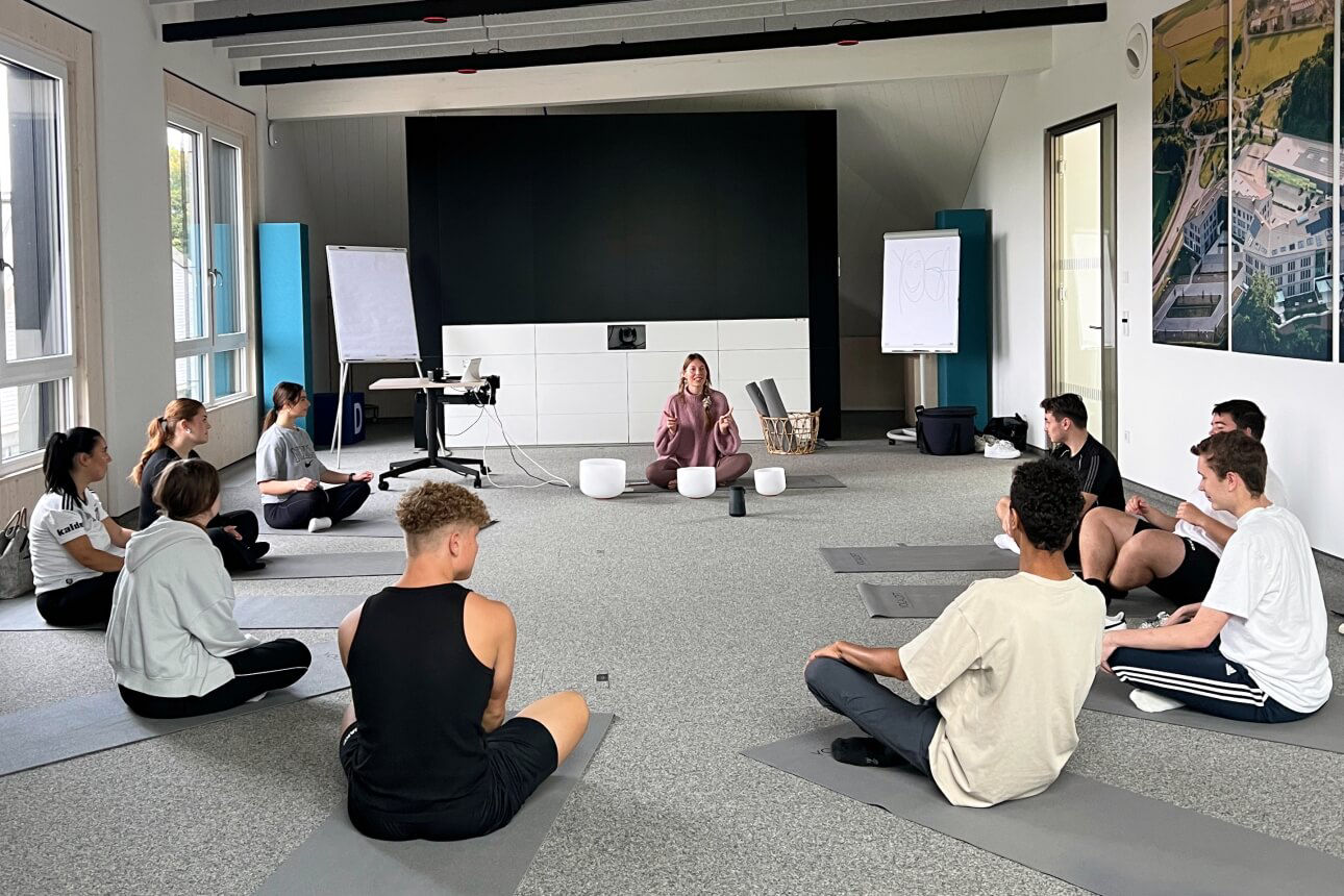 Unsere Azubis sitzen auf dem Boden im Kreis mit der Yogalehrerin