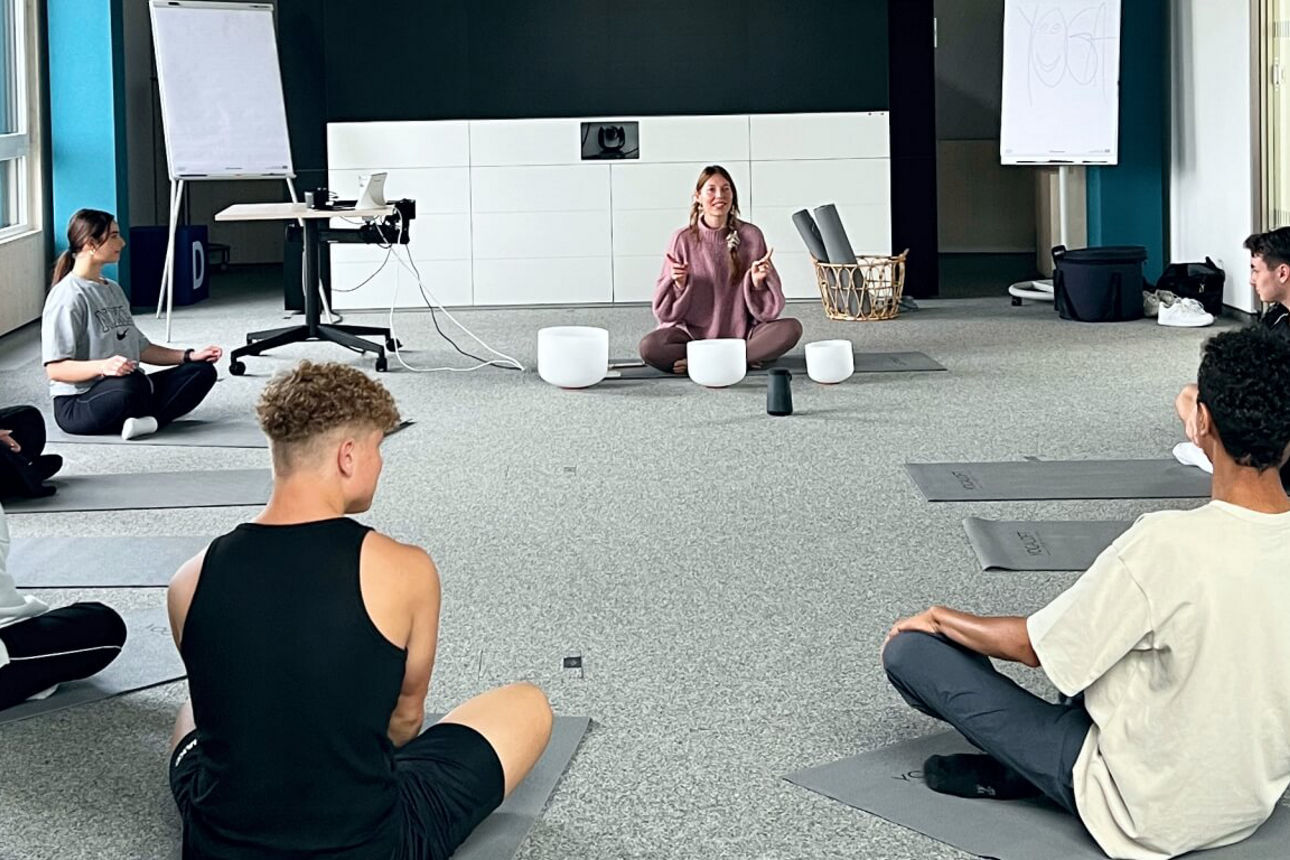 Unsere Azubis sitzen auf dem Boden im Kreis mit der Yogalehrerin