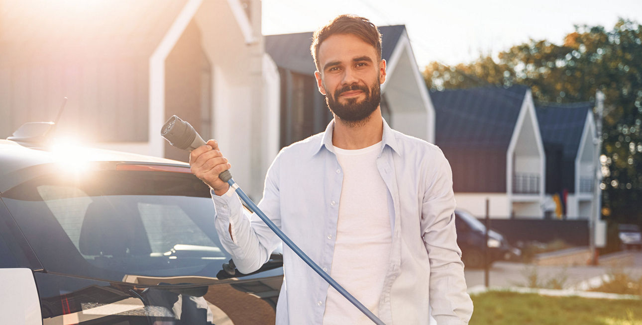 Mann mit Ladekabel steht vor E-Auto 