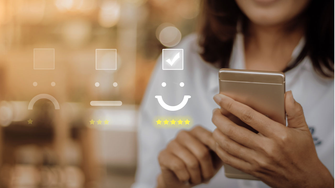 Eine Frau hält ein Handy in der Hand und im Bild sind drei Smilie-Gesichter zu sehen.