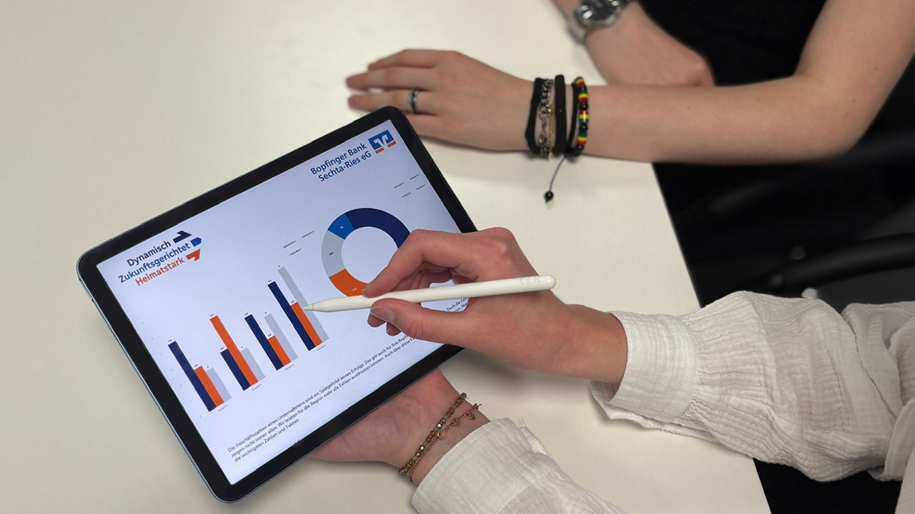 Ein Paar Hände hält ein Tabelt und ein Stift für das Tablet, auf dem Tablet sind zwei verschiedene Zahlendiagramme zu sehen.
