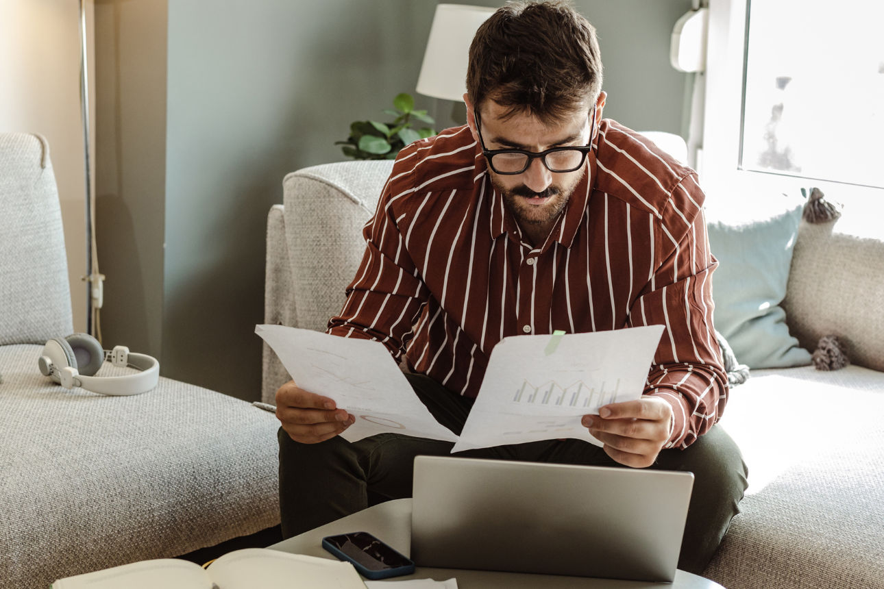 Ein Mann sitzt im Wohnzimmer auf dem Sofa und schaut sich seine Dokumente an. 