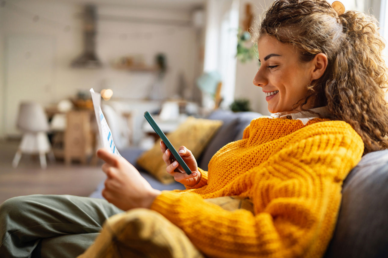 Darstellung einer lächelnden Frau, die auf einer Couch sitzt und ihr Handy in der Hand hält.