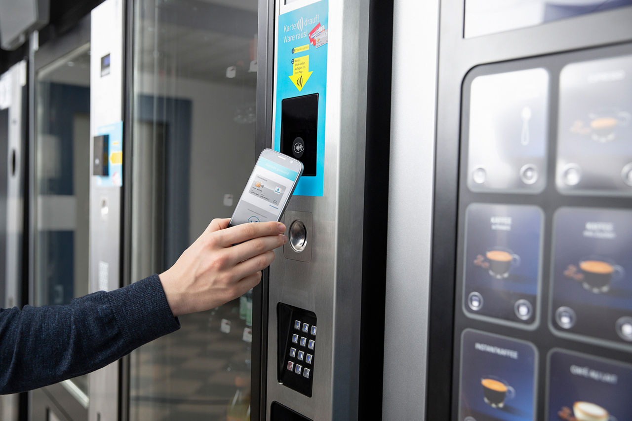 Jemand zahlt an einem Getränkeautomaten mit dem Smartphone