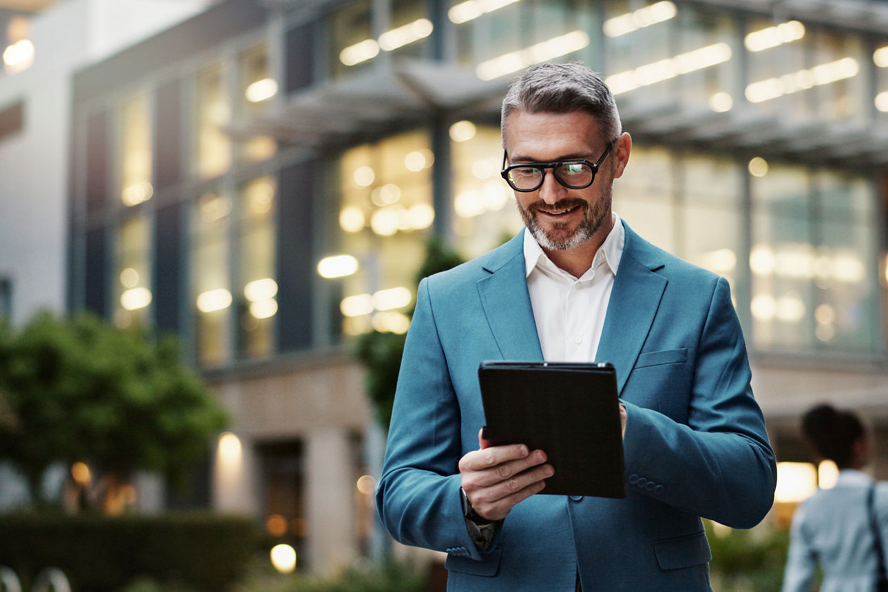 Mann vor einem Business Gebäude mit einem Tablet in der Hand 