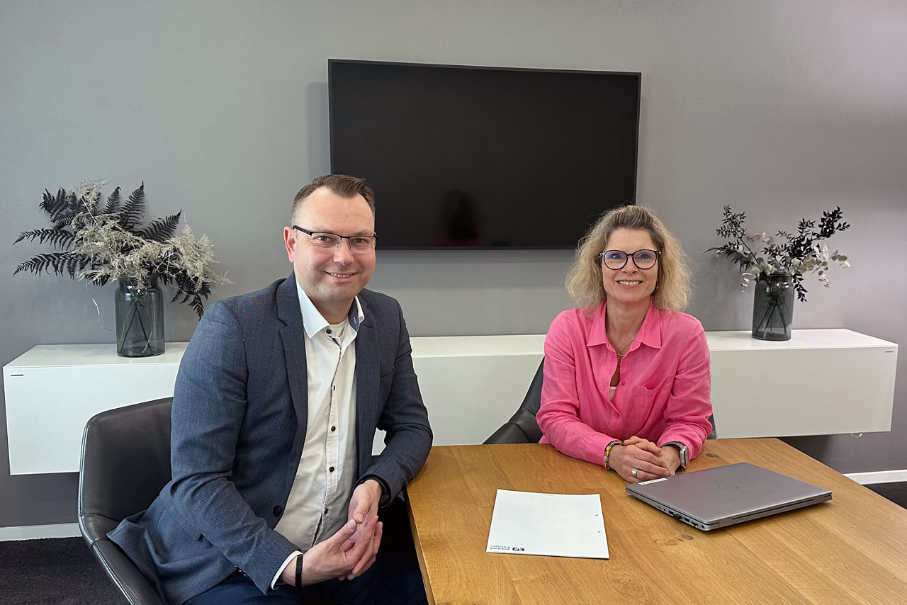 Unsere Zahlungsverkehrsberater Markus Thome und Nicole Lippold sitzen an einem Tisch und lächeln.