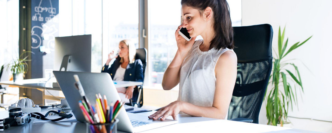 Junge Frau sitzt am Schreibtisch und telefoniert