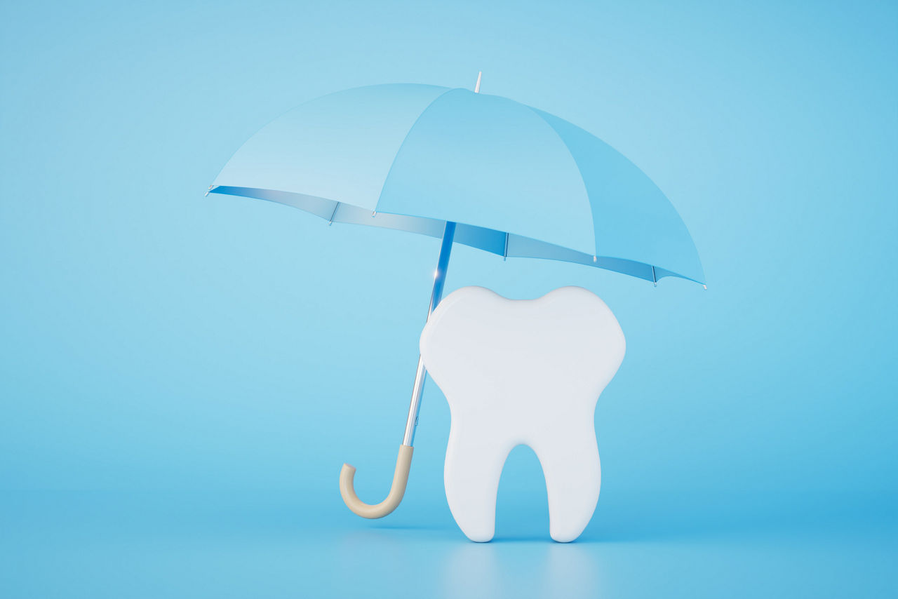 Ein Zahnmodell steht unter einem blauen Regenschirm als Symbol für Zahnschutz.