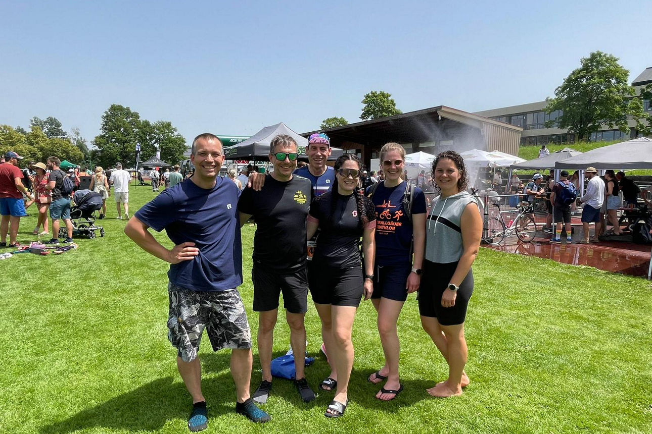 Mitarbeiter stehen Arm in Arm in Sportkleidung auf dem Sportgelände