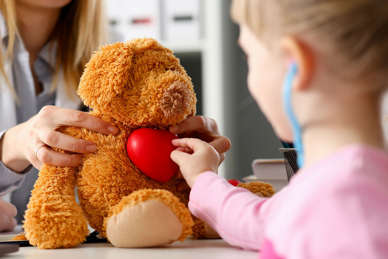 Kleines Kind in der Kinderarztpraxis untersucht das rote Herz eines Kuscheltierbären