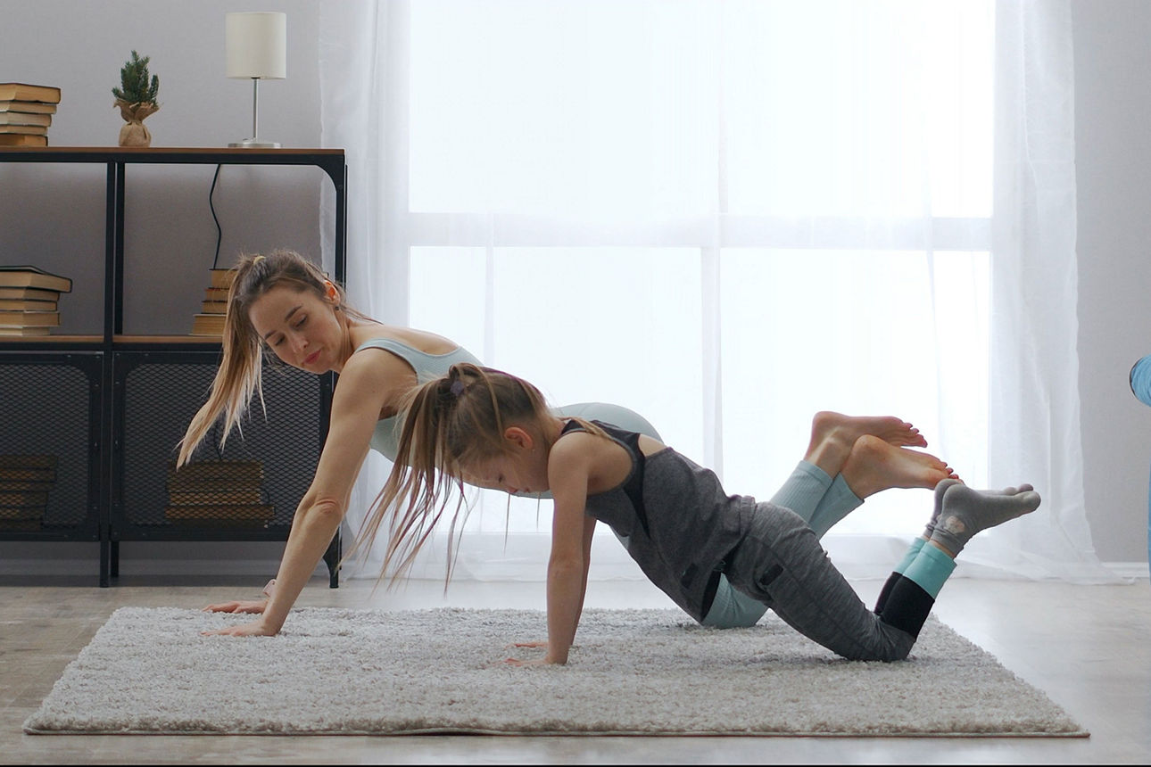 Zwei Personen machen in einem Wohnzimmer auf einem Teppich gemeinsam Fitnessübungen