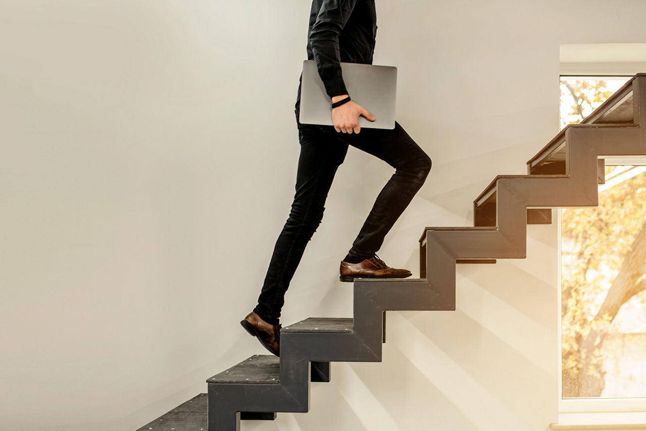 Mann geht mit einen Laptop die Treppe hoch