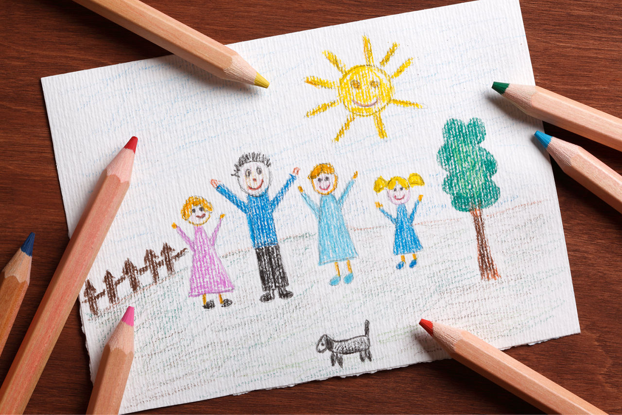 Ein von einem Kind bemaltes Papier mit dem Bild einer Familie und am Rand liegende Bundstifte