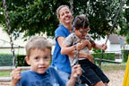 Das Bild zeigt eine Mama mit ihren zwei Kids beim Schaukeln auf einem Spielplatz.