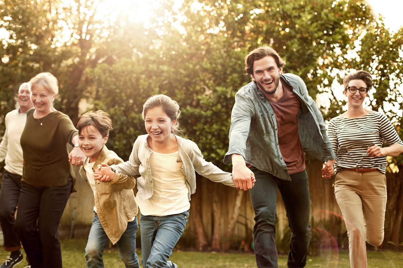 Familie hält sich an den Händen und rennt über eine Wiese