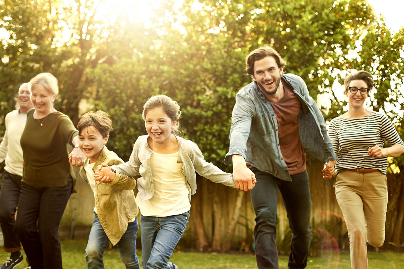 Familie hält sich an den Händen und rennt über eine Wiese