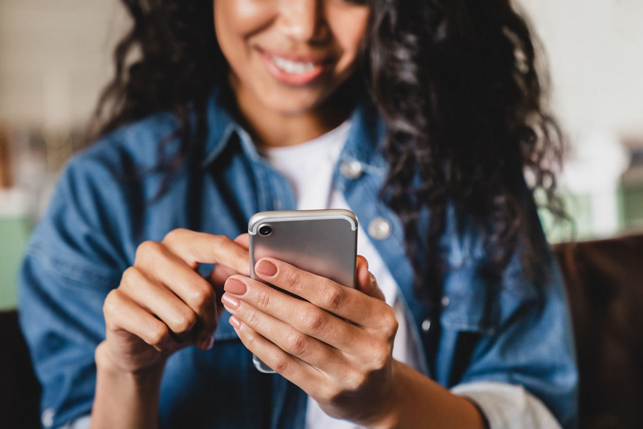 Eine junge Frau schaut lächelnd auf ihr Handy