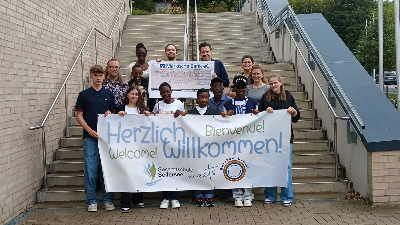 Schüler mit dem Zuwendungsscheck und einem Herzlich Wilkommen-Plakat in der Hand
