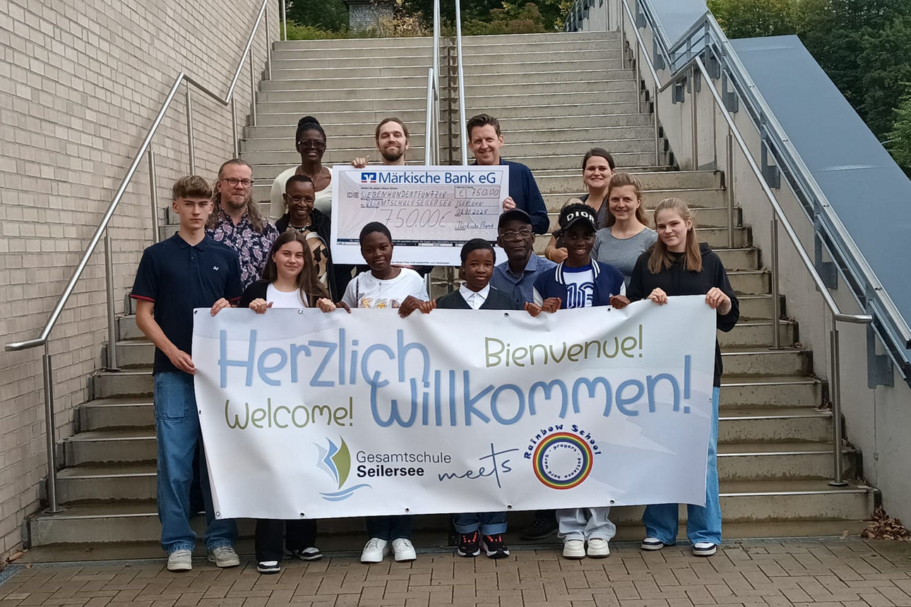 Schüler mit dem Zuwendungsscheck und einem Herzlich Wilkommen-Plakat in der Hand