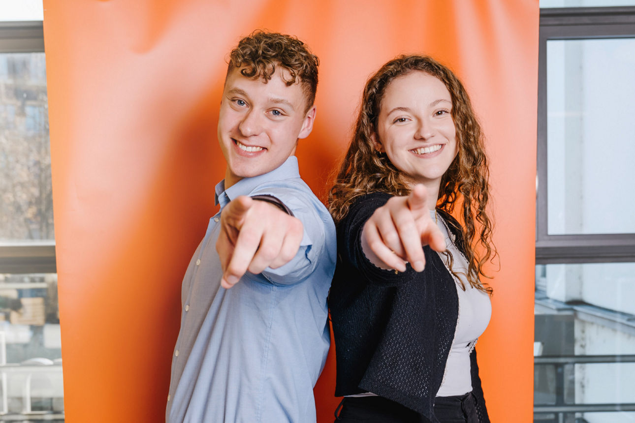 Zwei Auszubildende stehen Rücken an Rücken und deuten in Richtung Kamera
