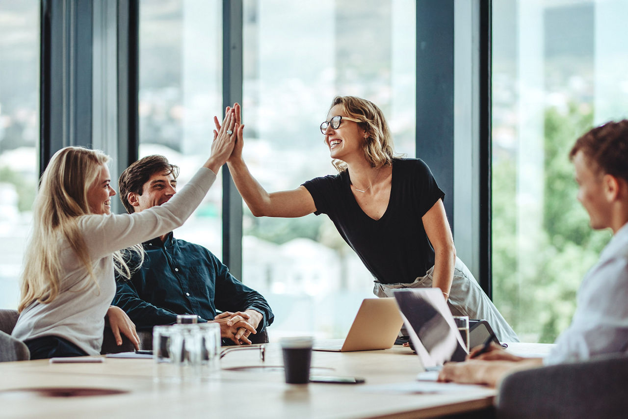 Zwei Frauen geben sich "High five" und freuen sich mit ihren männlichen Kollegen über einen Erfolg