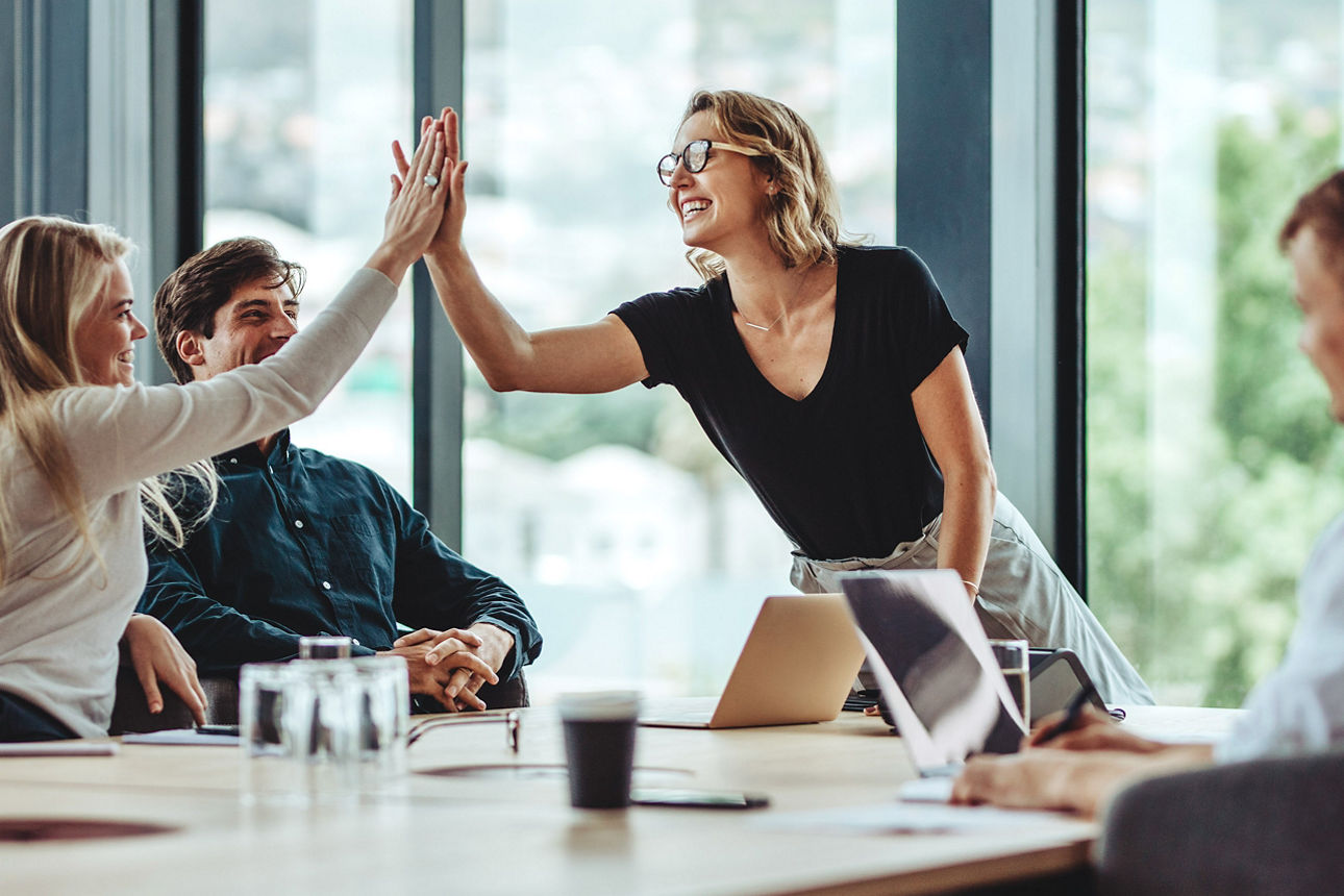 Zwei Frauen geben sich "High five" und freuen sich mit ihren männlichen Kollegen über einen Erfolg