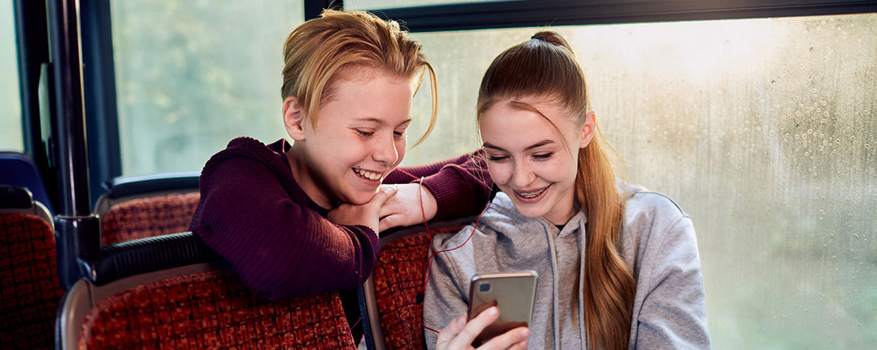 Zwei Jugendliche im Bus schauen auf ein Smartphone