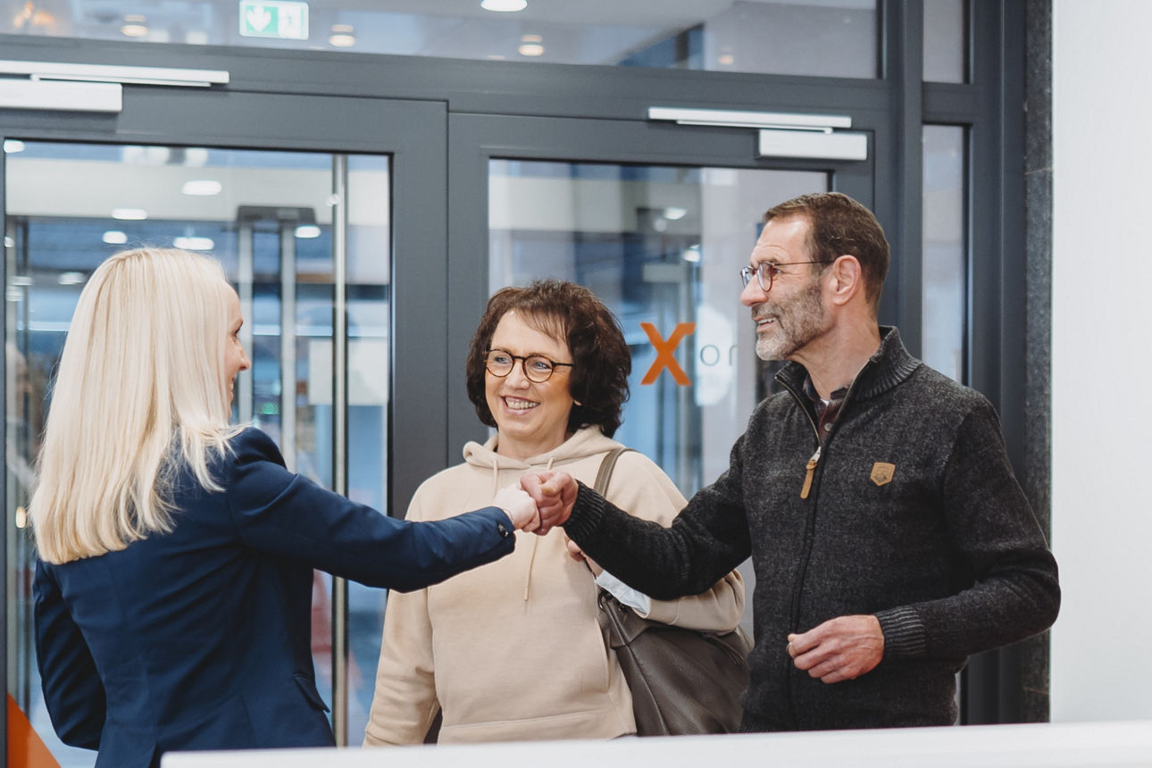Ein Mann und eine Frau schütteln sich die Hand. Daneben steht eine weitere Frau. Es sieht aus, als würden sie sich begrüßen. 