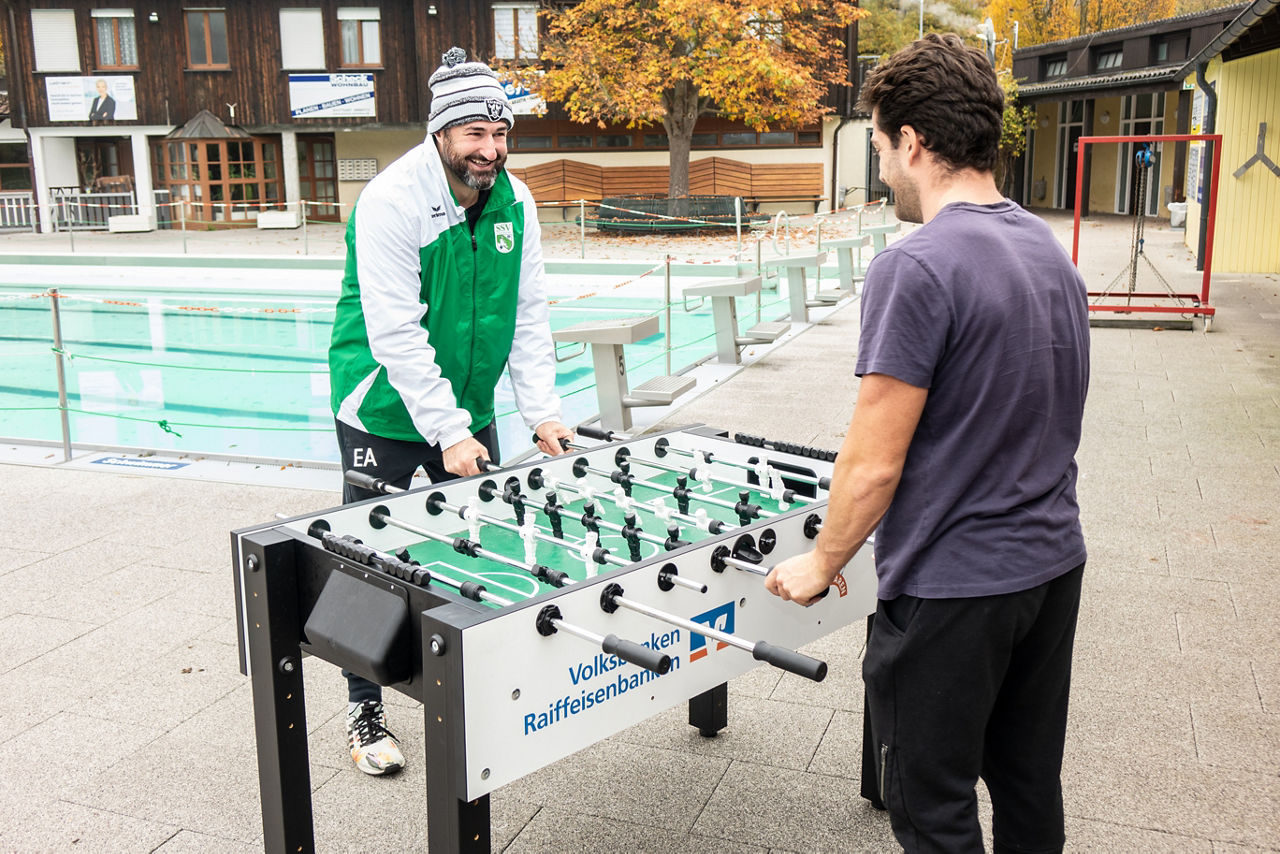 Zwei Männer spielen Tischkicker in einem Freibad