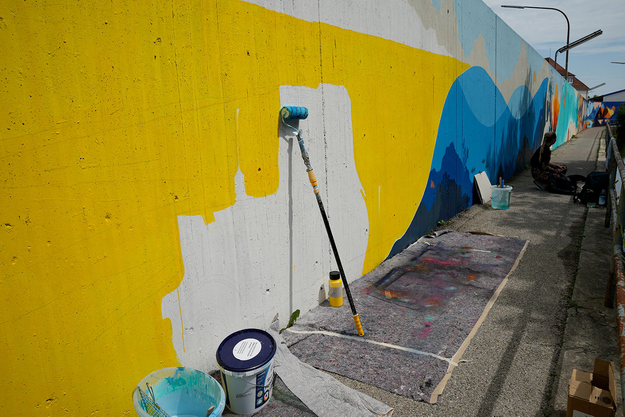 Ein blau-gelbes Kunstwerk entsteht auf einer Betonmauer