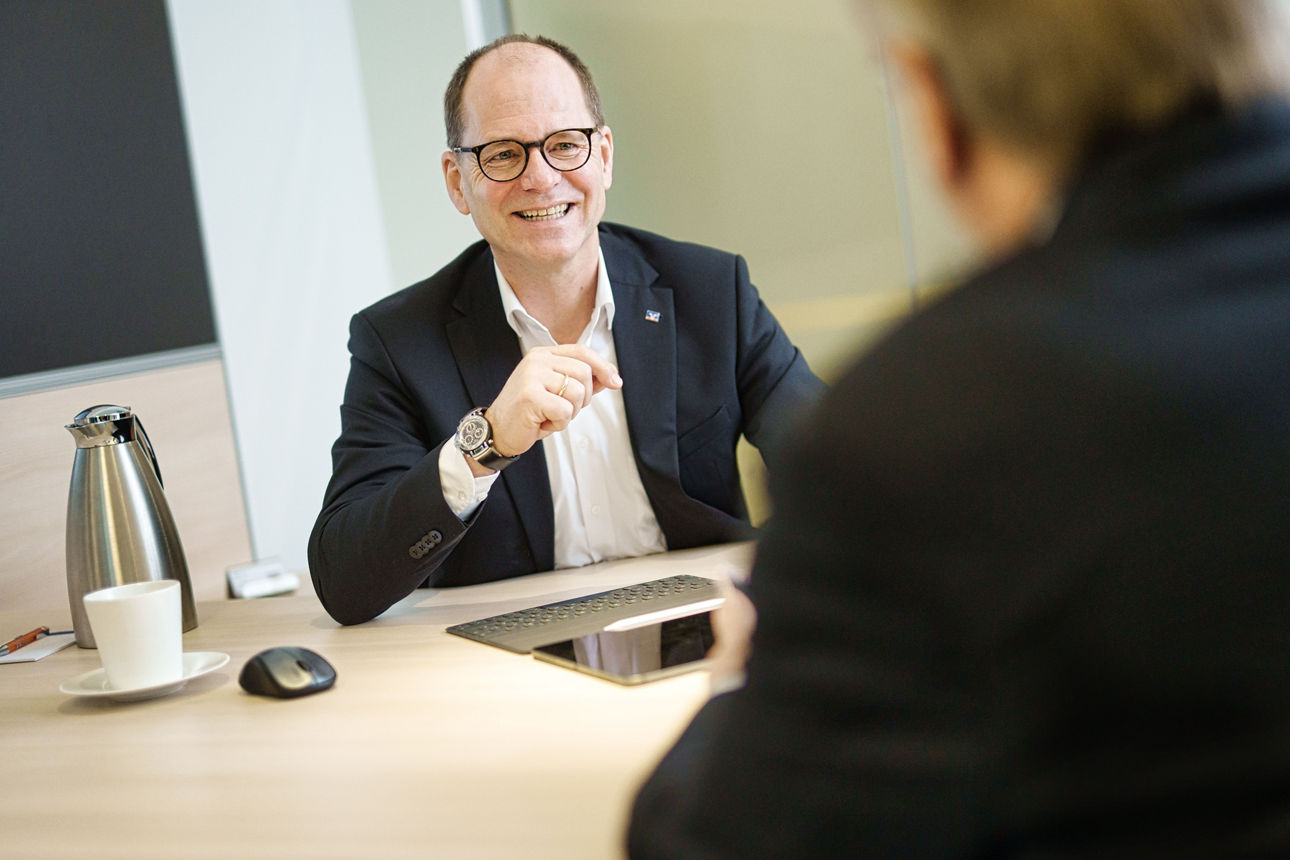Kundenbetreuer sitzt Kunden im Büro gegenüber und lächelt ihn an