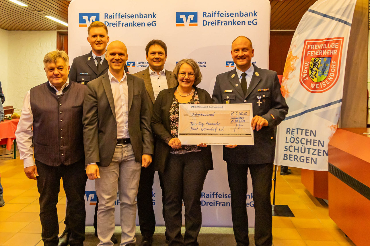 Vorstände der Feuerwehr, der Bank und Kundenberater präsentieren einen Scheck in Höhe von 7.000 Euro